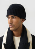 A close-up of a model wearing the Percival black ribbed wool beanie, paired with a cream knit scarf and a black coat.