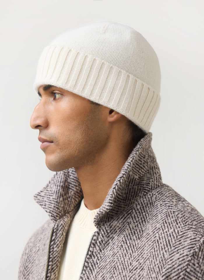 A man models the Percival ecru wool beanie in profile, paired with a herringbone jacket.