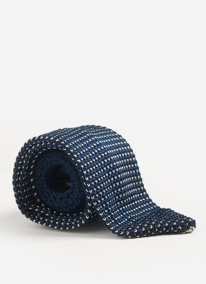 The Percival Birdseye Silk Tie in blue, rolled up to showcase its textured knit pattern against a clean white background.