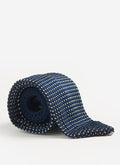 The Percival Birdseye Silk Tie in blue, rolled up to showcase its textured knit pattern against a clean white background.