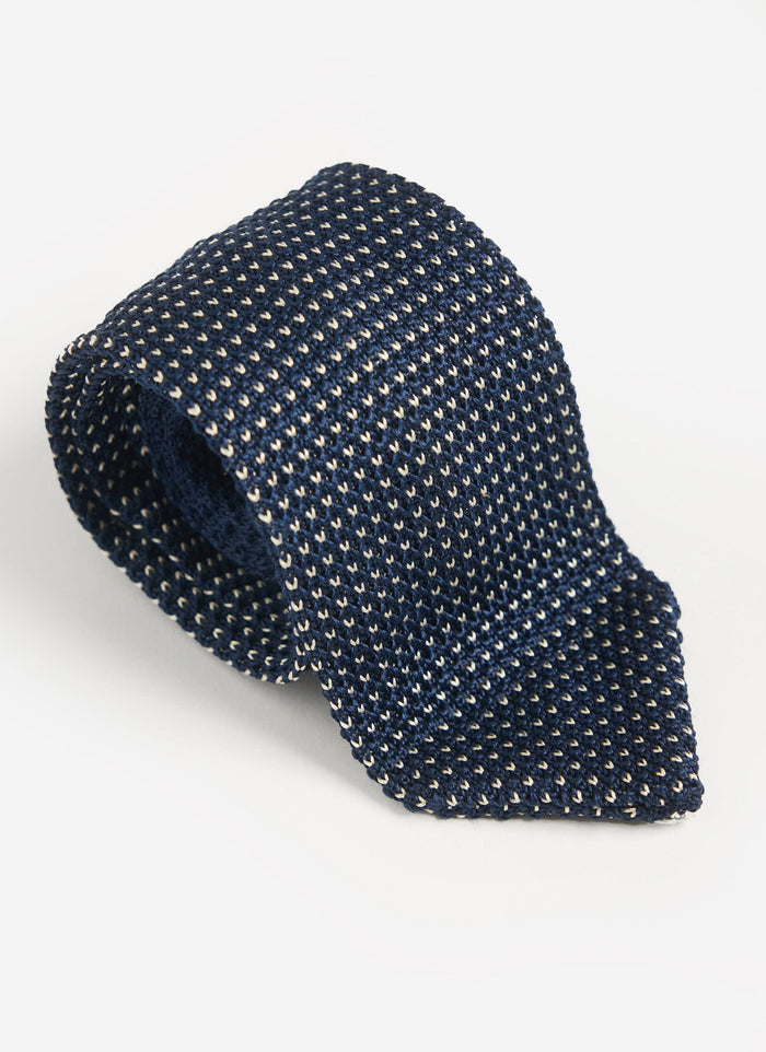 A studio shot of the blue Birdseye Silk Tie by Percival, coiled to show the textured diamond knit pattern.
