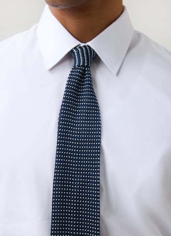 A close-up of a model wearing the blue Birdseye Silk Tie from Percival, paired with a crisp white shirt.