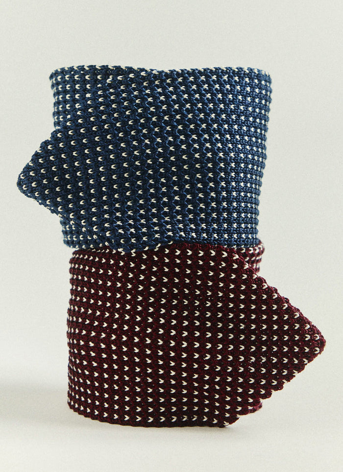 The red and blue Percival Birdseye Silk Ties, rolled and stacked to display their intricate textured knit.