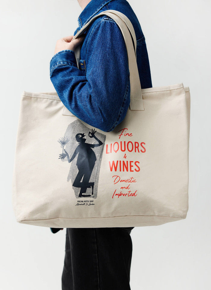 A model wears the Percival Carlo Mixologist tote bag in ecru, carried over the shoulder of a blue denim jacket.