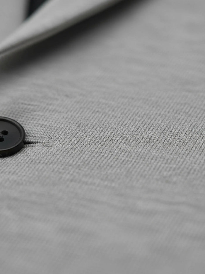 Close-up texture of light grey blazer fabric with button detail.