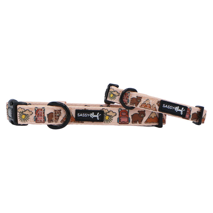 Two beige Sassy Woof "Dog Collar - National Bark" neoprene collars with camping-themed prints—tents, trees, lanterns, flowers—plus black buckles, D-rings, and brand label. Perfect outdoor dog accessories.