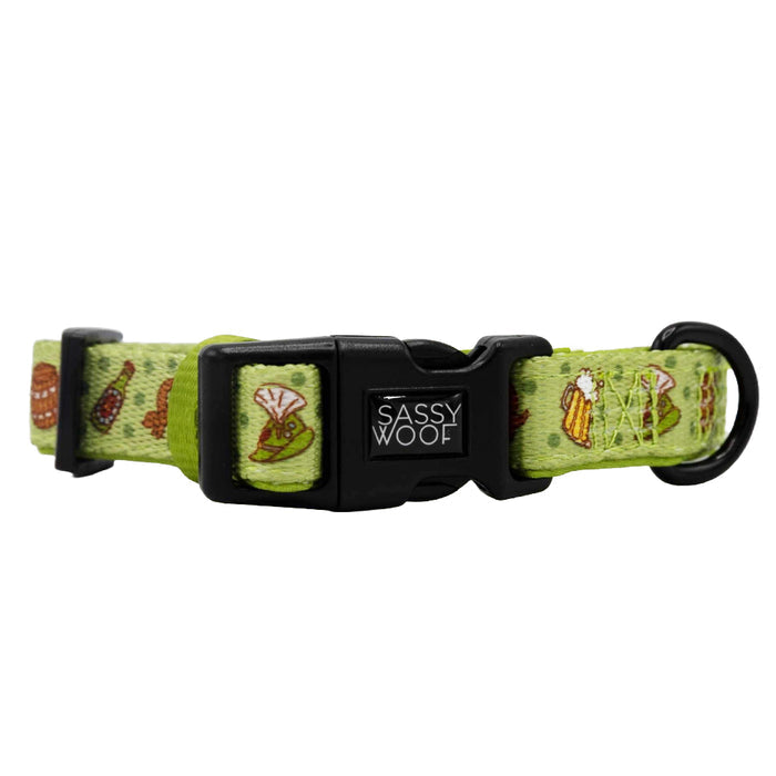 The Sassy Woof Dog Collar - Wurst Behavior is light green, adjustable, features a black plastic buckle and ring, and is decorated with colorful embroidered vegetables and the Sassy Woof brand name on the buckle.