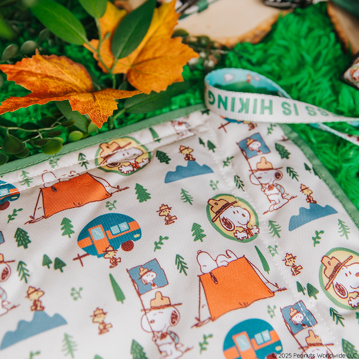 The Sassy Woof Dog Picnic Blanket – Peanuts™ Beagle Scouts features Snoopy in a ranger hat with camping-themed designs, including tents, trees, green leaves, and an orange leaf—perfect for outdoor pet gear or Snoopy dog accessories.