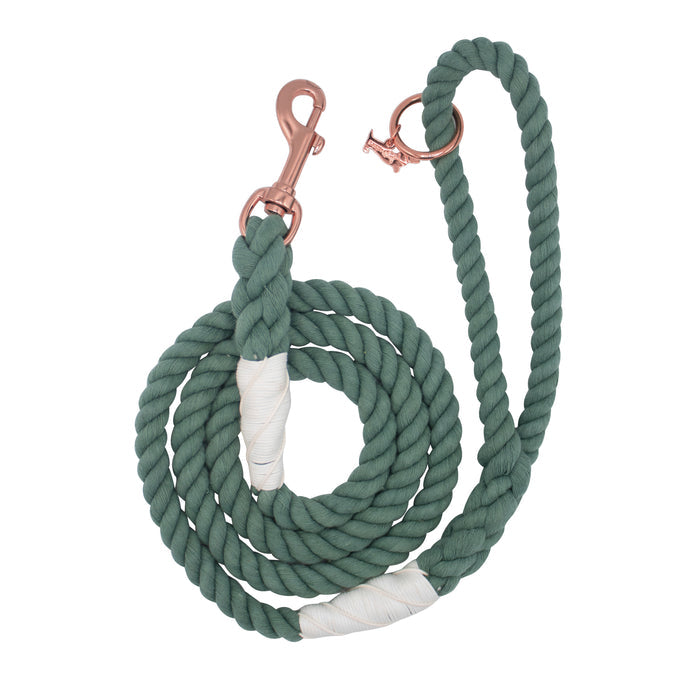 The Sassy Woof Dog Rope Leash - Amazon is a hand-crafted green cotton rope dog leash with white wrapped accents and a rose gold metal clip, shown coiled neatly on a white background.
