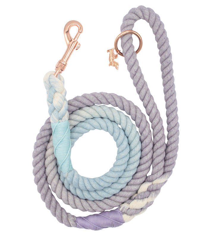 The Sassy Woof Dog Rope Leash - Skyfall features hand-crafted ombre lavender, blue, and white rope with a rose gold metal clasp and a delicate rose gold dog charm by the handle.
