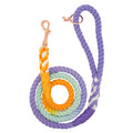 The Sassy Woof Dog Rope Leash - Sunset is a hand-crafted cotton leash with purple, yellow, white, and light blue ombre sections, featuring a brass clasp and a coiled spiral design with a loop handle.