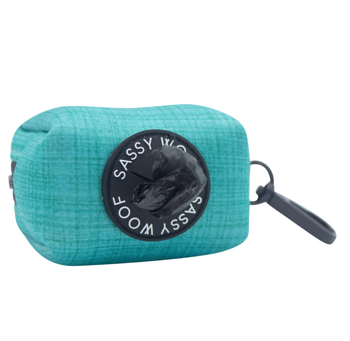 The Sassy Woof Dog Waste Bag Holder - Napa features teal neoprene, a black circular brand label, a gray clip for easy carrying, and is inspired by Napa Valley as part of the luxurious green collection.