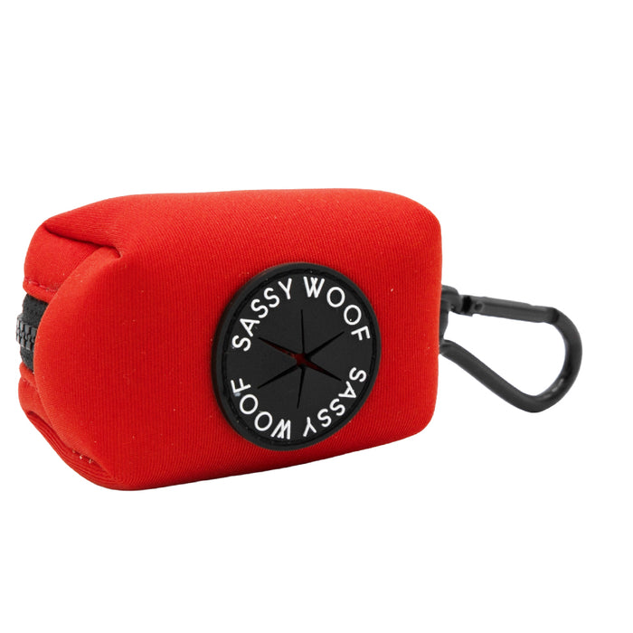 The Sassy Woof Dog Waste Bag Holder in neon red features durable neoprene, a black zipper, a round dispenser, and a black clip—perfect for easy bag dispensing and matching your dog's harness on every walk.