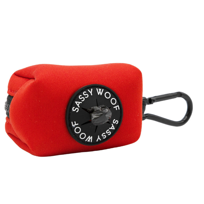The Sassy Woof Dog Waste Bag Holder in Neon Red is made of durable neoprene with a black zipper, plastic clip, and round logo. It matches your harness set and dispenses bags easily through the center hole.