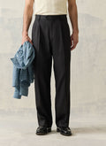 Black double pleated lyocell blend trousers by Percival, styled on a model with black loafers and a blue checked shirt.