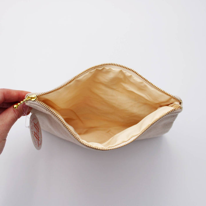 Beige canvas pouch interior with tan lining and gold zipper edge, held in hand