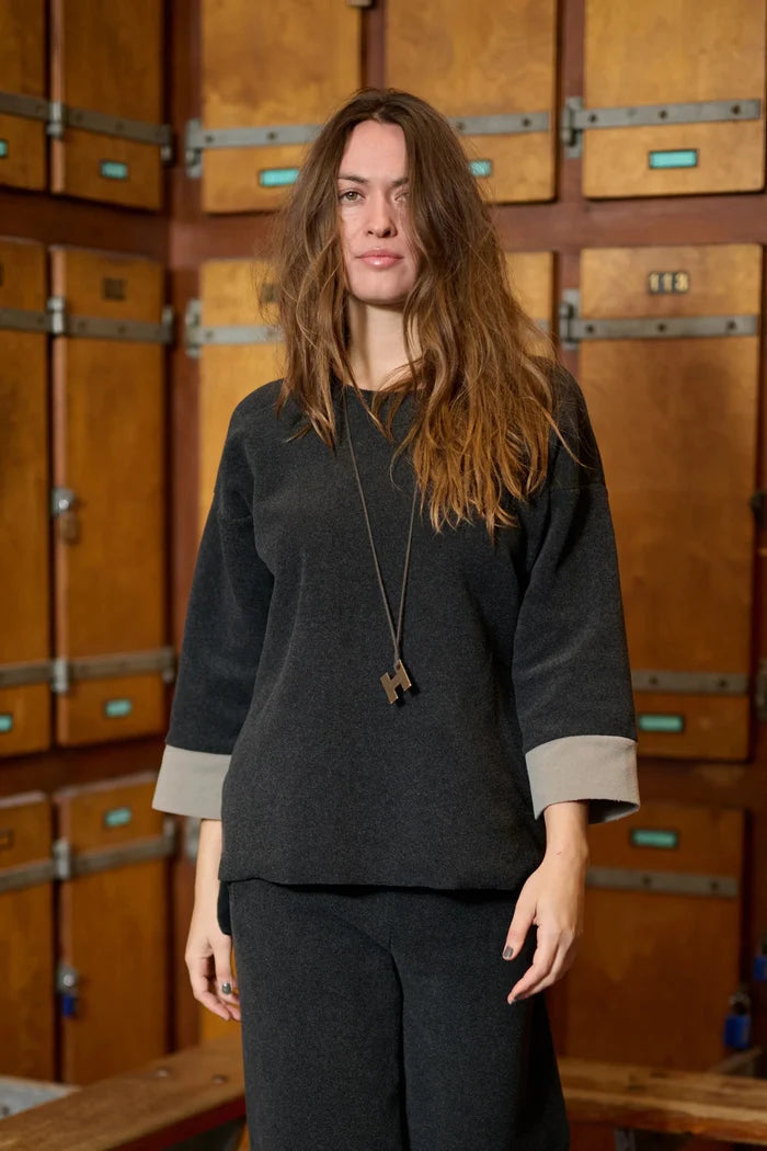 Woman wearing a dark gray outfit standing in front of wooden lockers.