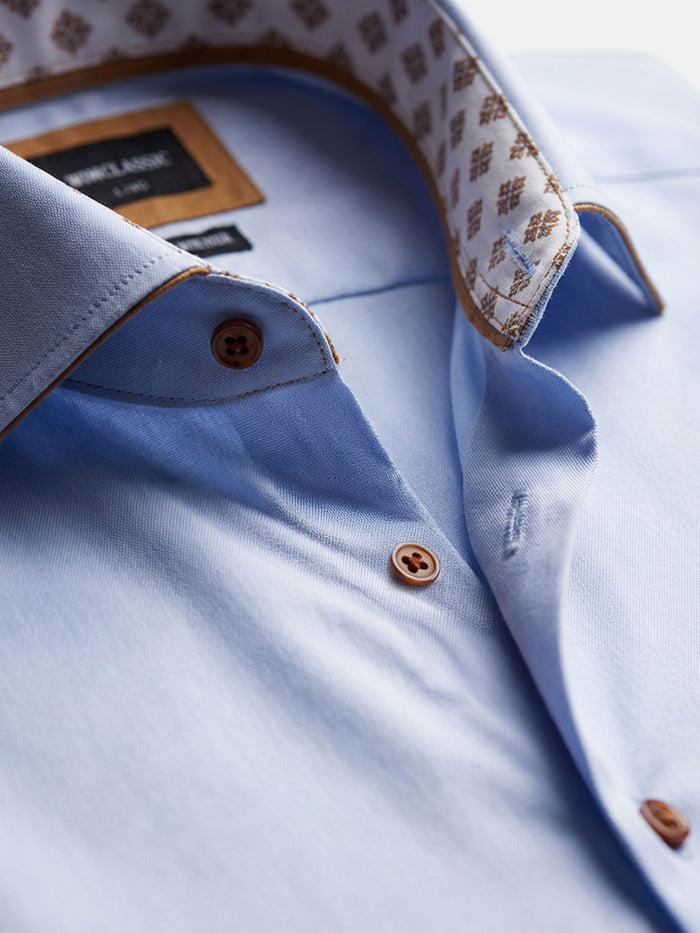 Close-up of light blue men’s shirt collar with contrast buttons and patterned lining