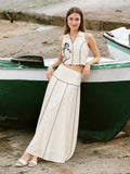Woman in a stylish outfit standing next to a boat on a beach.