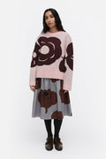 Woman wearing a pink sweater with brown floral patterns and a gray skirt on a white background