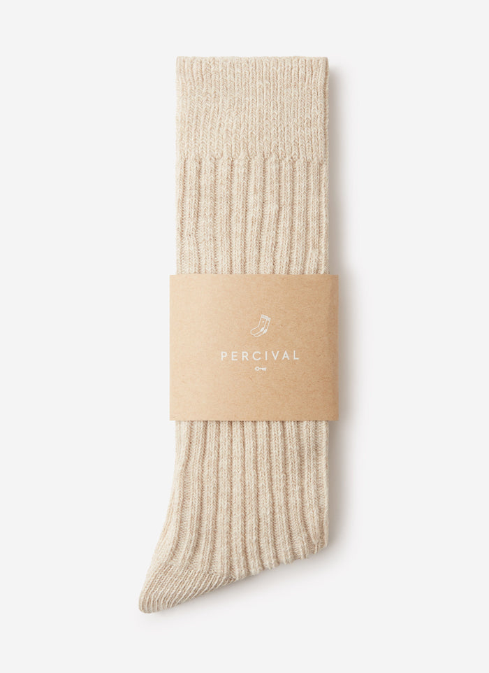 A pair of ribbed Percival Marl Socks in oat, folded and presented in a branded cardboard sleeve against a white background.
