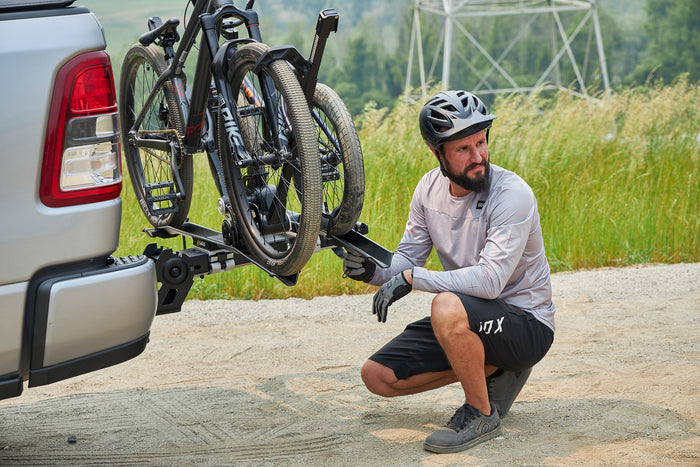 Cyclist securing rear wheel on Saris MHS UNO Modular Hitch Rack at trailhead