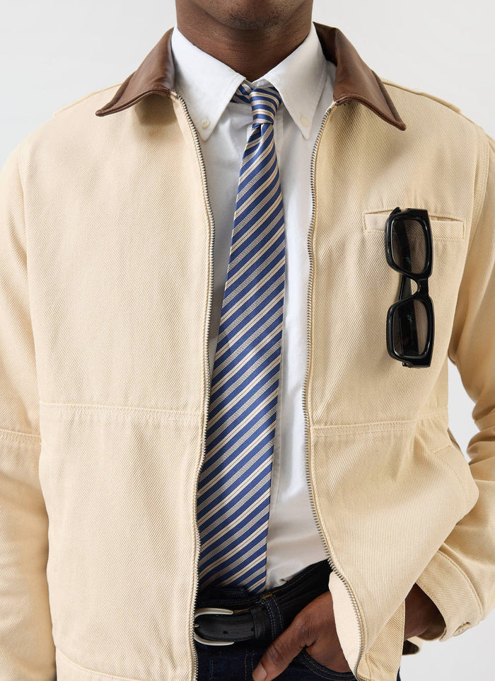 A close-up shot of a model wearing the Percival Micro Stripe Silk Tie with a crisp white shirt and a beige zip jacket.