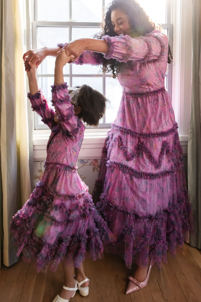 A woman and a young girl wearing matching Ivy City Co Mini Catherine Dresses in Climbing Vine Bloom dance by a sunlit window, smiling and holding hands—capturing sweet matching moments.
