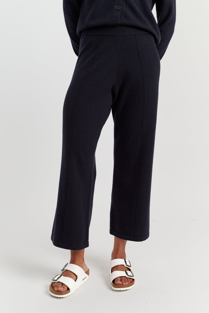 Person wearing black pants and white sandals on a light grey background
