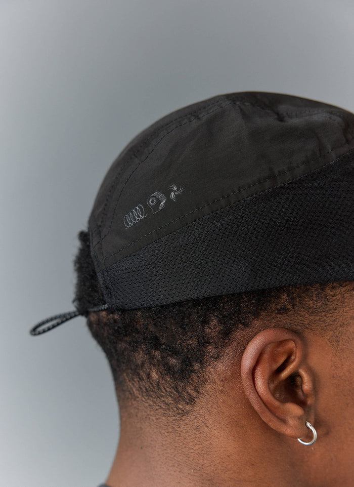 A close-up side view of the black PCVL Nylon Cap from Percival, showing the tonal logo embroidery and performance mesh panel.