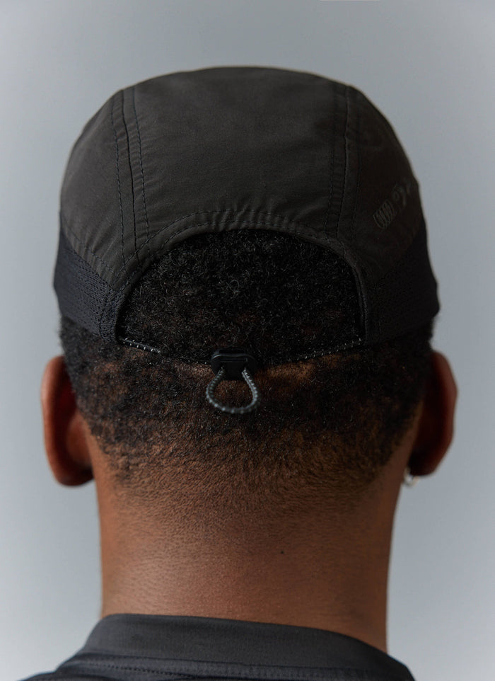 A close-up view from behind of a model wearing the black PCVL Nylon Cap from Percival, showing the toggle fastener.