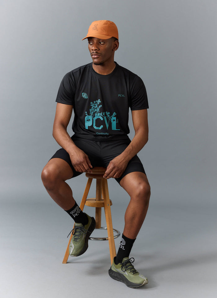 A model wears the rust PCVL Nylon Cap with a black graphic t-shirt and shorts from the Percival performance wear range.