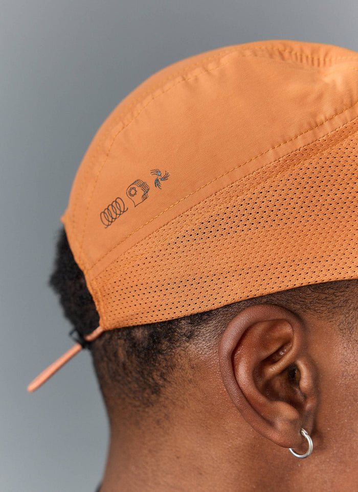 Close-up of a model wearing the rust PCVL Nylon Cap from Percival, highlighting embroidered detail and breathable material.