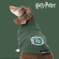 A brown dachshund models the Sassy Woof Pet Cable Knit Sweater - Harry Potter™ Slytherin, featuring a green cable knit design and iconic crest, against a plain green background.