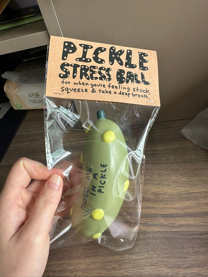 Pickle-shaped stress ball in retail package, light green ball visible through plastic