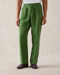 A model wearing Percival forest green pleated linen trousers with belt loops, paired with a white t-shirt and loafers.