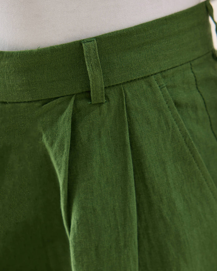 A close-up of the waistband and pleat detail on Percival forest green linen trousers with belt loops.