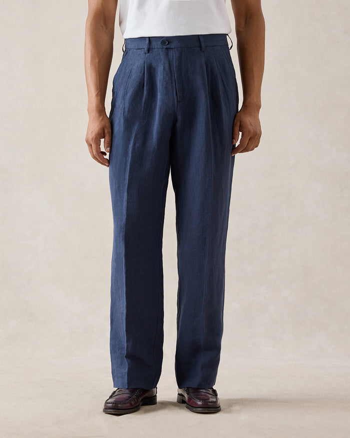 A model wears the navy blue Pleated Tailored Trousers from Percival, featuring belt loops, paired with a white t-shirt.