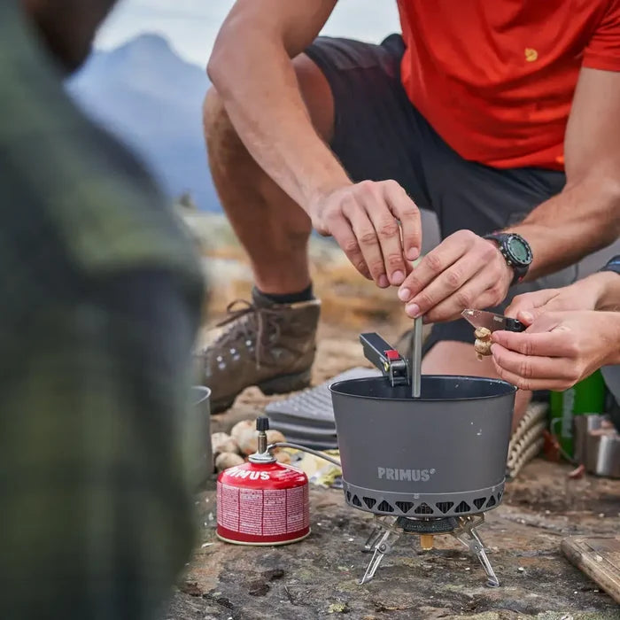 Person using a Primus Gravity Camping Gas Stove with a Primus pot outdoors with mountains in the background