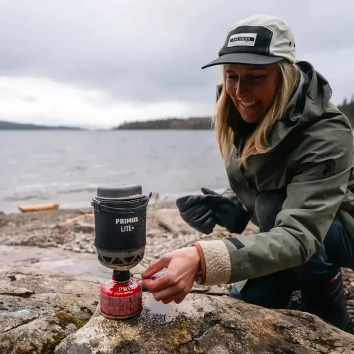 Person using a Primus Lite+ camping stove by a lake