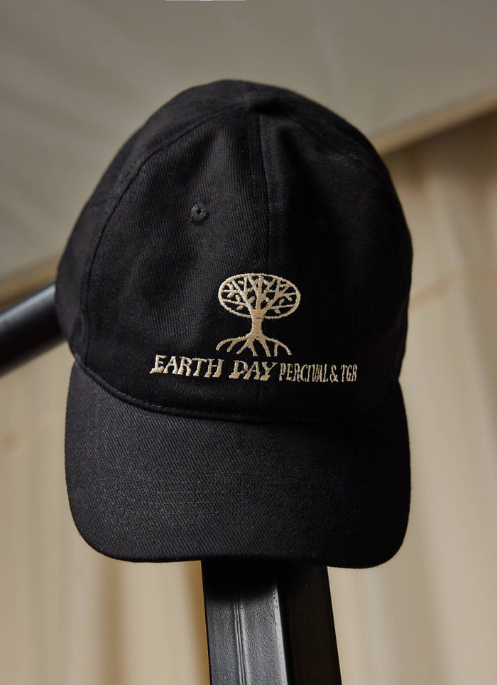 The Percival x The Gorilla Brand black cotton cap, featuring Earth Day embroidery, resting on a black rail.