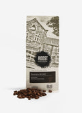 A bag of the Percival x Roost Espresso coffee blend, with roasted beans scattered in front against a white background.