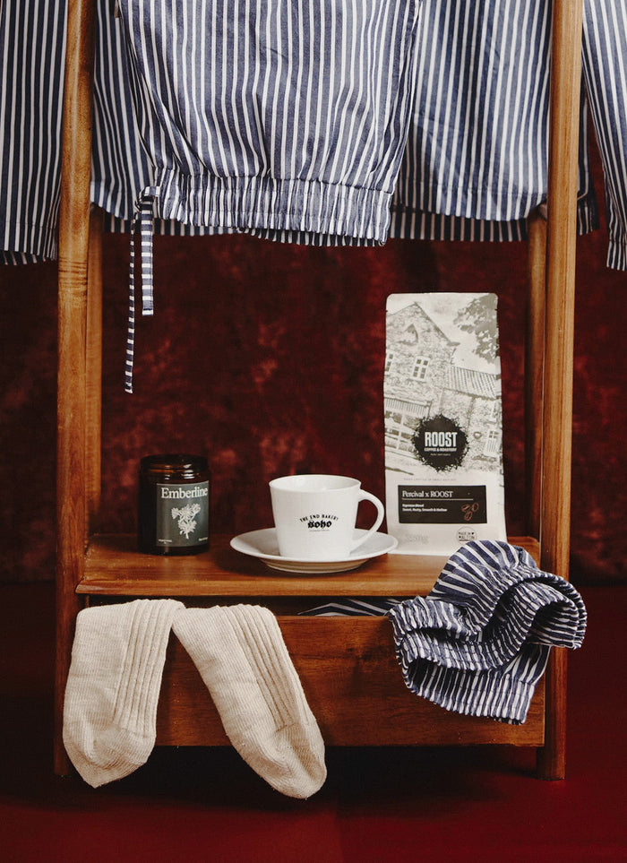 Percival's Roost Espresso Coffee displayed on a wooden stand with striped pyjamas, socks, and a mug for the perfect morning.