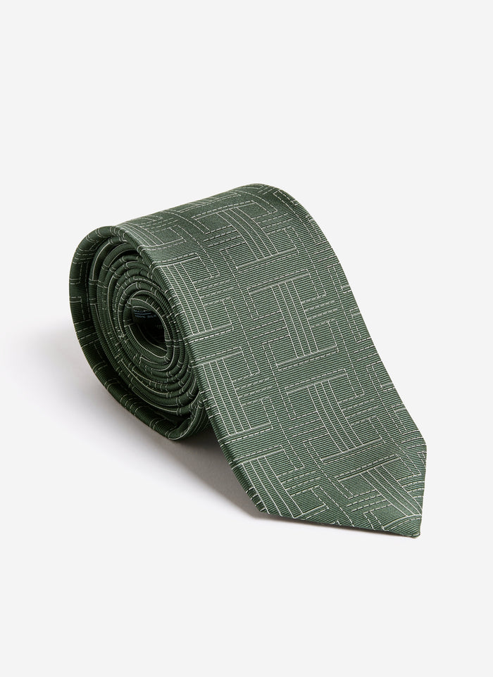 The Percival Sashiko Tie in forest green silk, rolled up to display its intricate geometric weave on a white background.