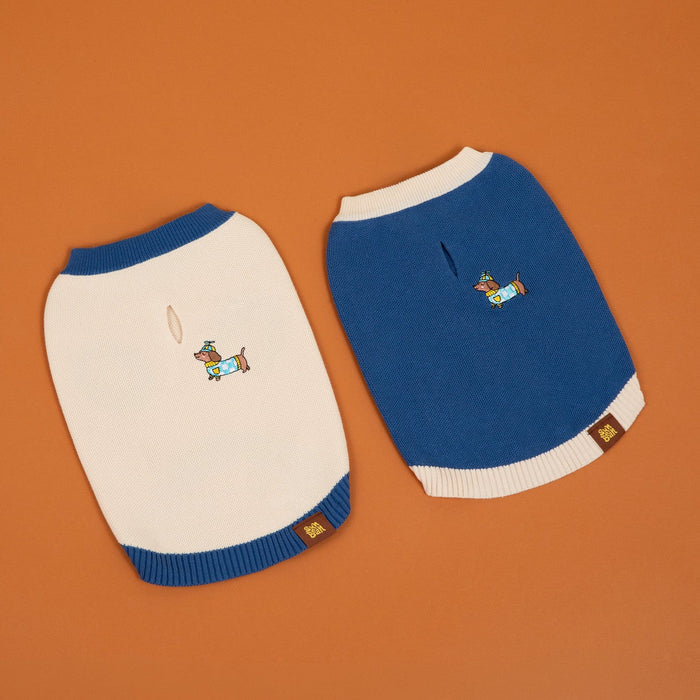 Two small Sassy Woof x Sunbean Dog Tees by Sunbean—one in cream with blue trim and one in blue with cream trim—each featuring an embroidered dog in a hat and scarf, displayed on an orange background. Ideal for those who love matching outfits with their dogs or are fans of the adorable Sassy Woof x Sunbean collaboration.