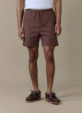 A model wearing the Percival Sorrento Shorts in brown linen, featuring a subtle vertical stripe and drawstring waistband.