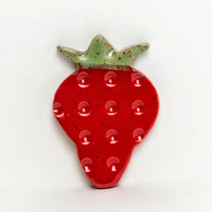 Strawberry-shaped red ceramic refrigerator magnet with green leafy top and speckled glaze