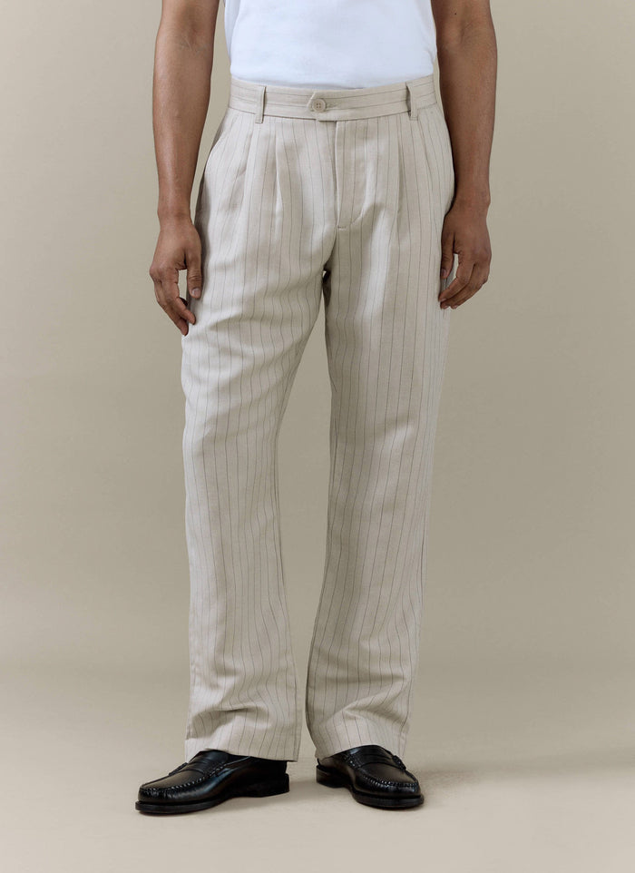 A model wears the cream striped pleated tailored trousers from Percival, styled with a white t-shirt and black loafers.