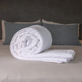 British Wool Summer Duvet 100% cotton handmade in the UK made to be hypo-allergenic, anti dust mite & sustainable. Rolled on a bed with visible cotton cover and Putnams tag, in a calm bedroom setting