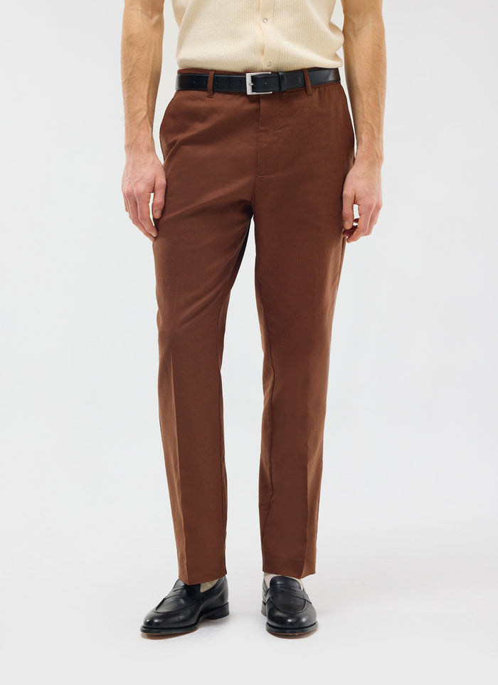 A model wears the Percival Tailored Linen Trousers in brown, styled with a black belt and loafers.